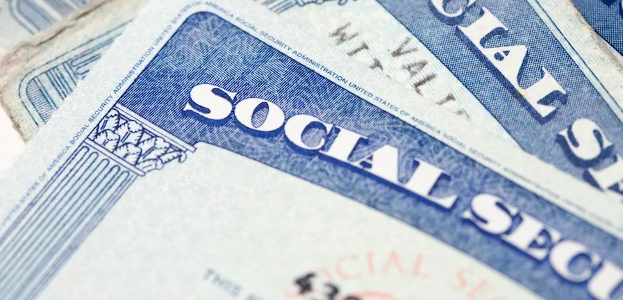 Close-up of multiple Social Security cards stacked slightly askew. Only part of the text "SOCIAL SECURITY" is visible on each card, showcasing the distinct blue color and design elements.